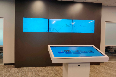 The three screen kiosk with some of the media hubs visible on the touch screen, and an idle animation on the screens above.